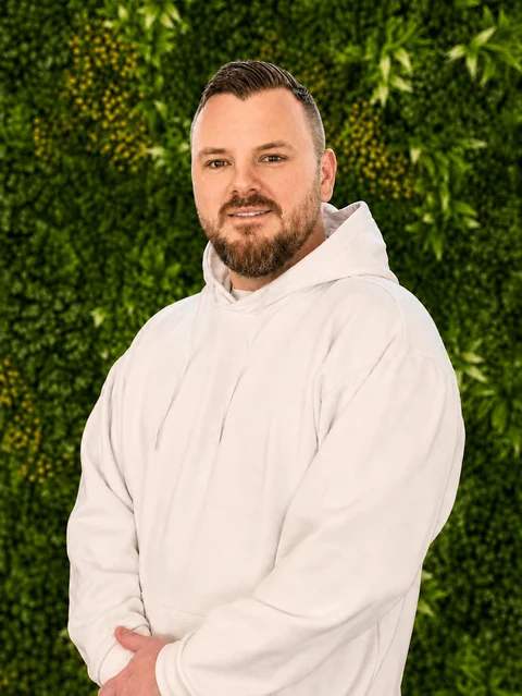 Tim Kelle in einem weißen Hoodie vor einer grünen Pflanzenwand